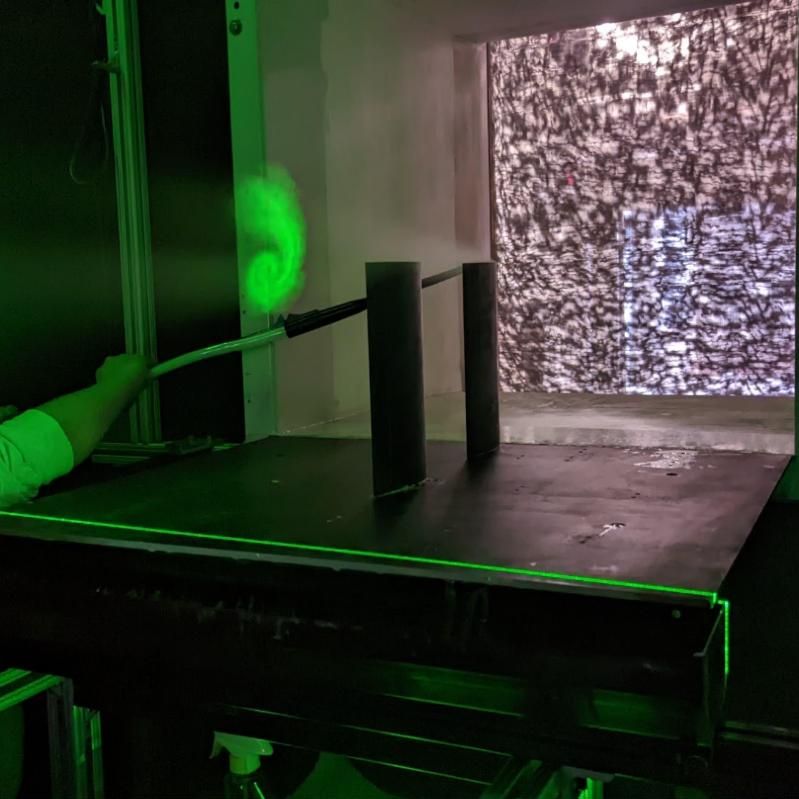 Wind tunnel test section lit by a green laser sheet, with smoke seeding the flow